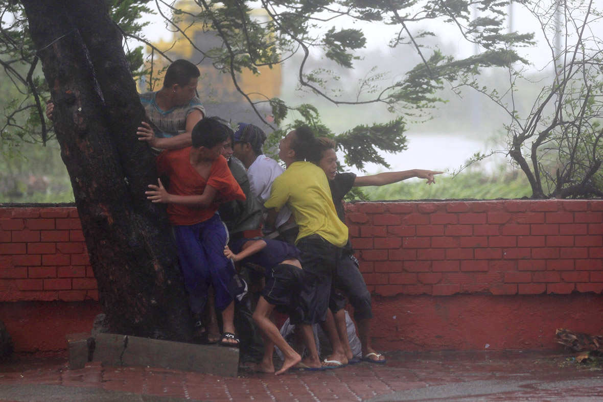 People take cover under a tree as strong winds brought by Typhoon Rammasun batter the capital.