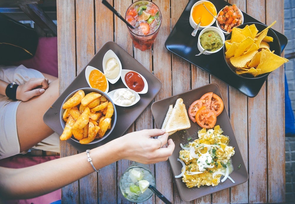 Womans Hand Taking Food From Cafe Table With Dips And Drinks