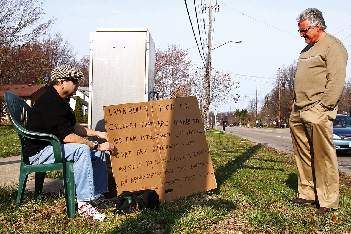 Edmond Aviv sits with a sign he made, on a street corner in South Euclid, a suburb of Cleveland, Ohio. A judge ordered him to display the sign as punishment for feuding with his neighbour and her adopted, disabled African-American children