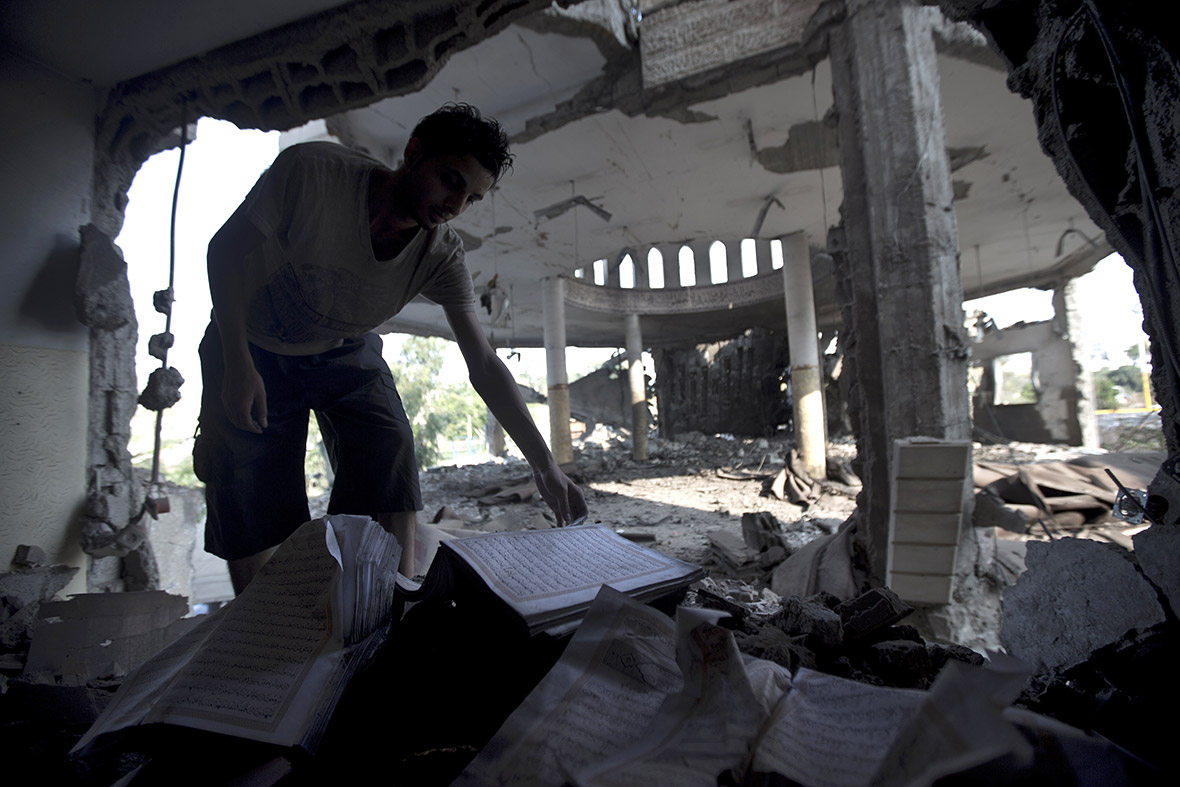 A Palestinian man looks at copies of the Koran, Islam's holy book, in the rubble of a mosque destroyed by an Israeli military strike in Gaza City