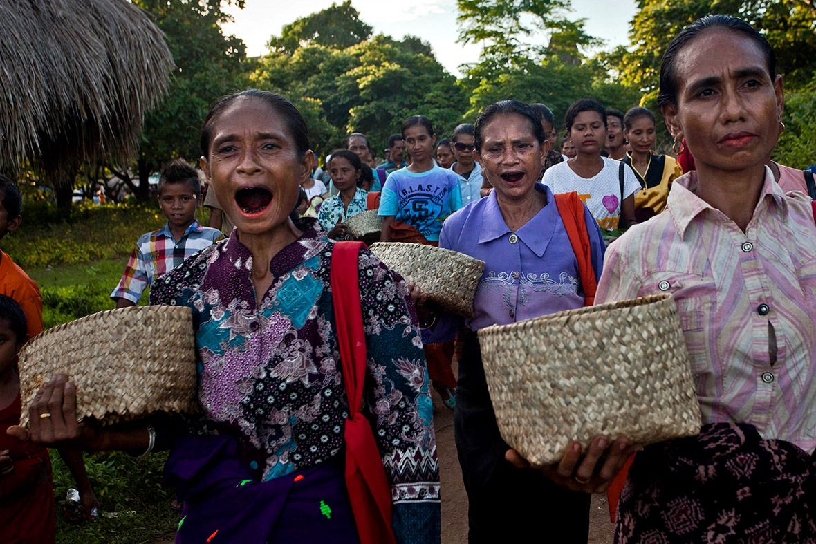 Villagers, their mouths stained with betel nut juice, perform a prayer ritual at the graves of their ancestors