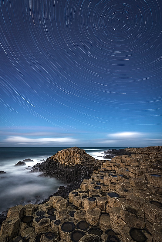 A Giant's Star Trail by Rob Oliver (UK). A composition of several images taken at the famed Giant's Causeway in Northern Ireland. Our planet's rotation draws the stars out into circles – considered to be the most perfect shape by ancient philosophers. Separated from the sky by the stark line of the horizon, the atomic symmetries of crystallised rock display themselves in the hexagonal columns of the Giant's Causeway.