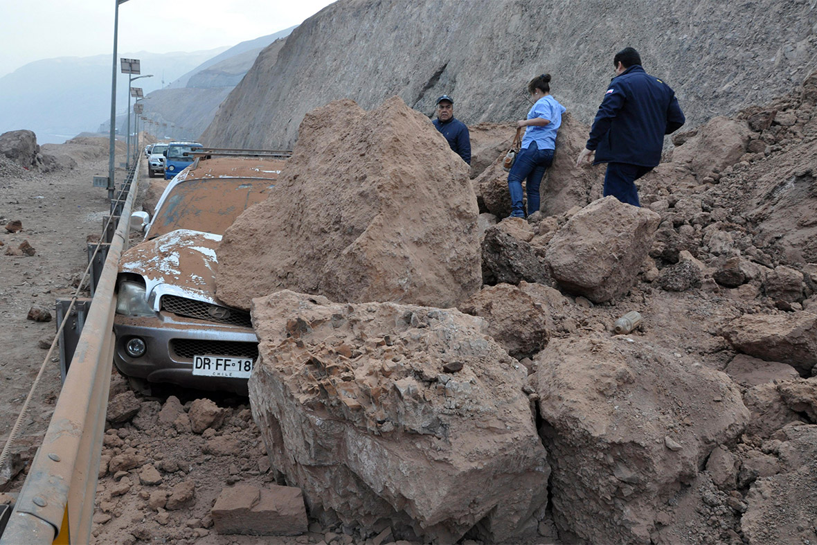 Rescue workers inspect a car caught under a landslide after an earthquake hit Iquique
