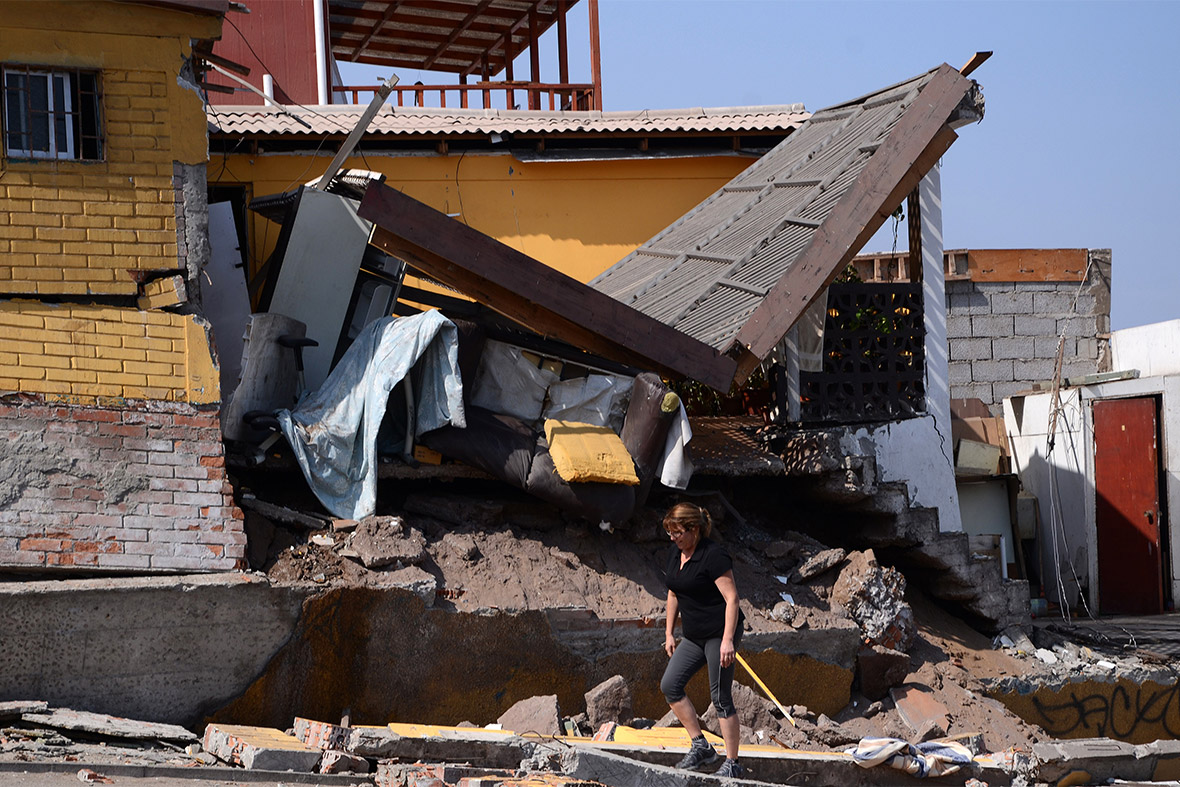 A woman walks past a destroyed house in Iquique