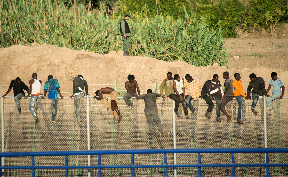 African migrants climb a border fence during an attempt to cross into Spanish territory between Morocco and Spain's north African enclave of Melilla