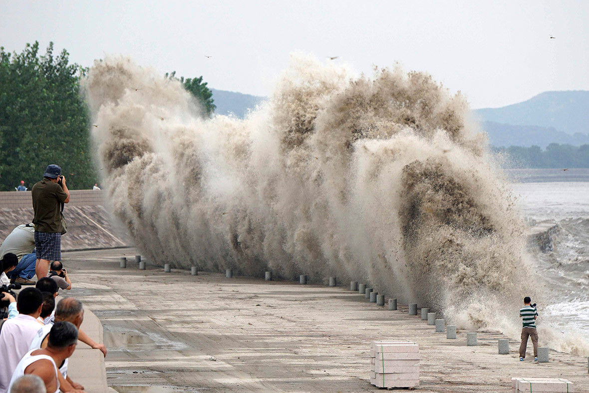 People take pictures and videos as tidal bores surge past a barrier on the banks of Qiantang River, in Jiaxing, Zhejiang province, China