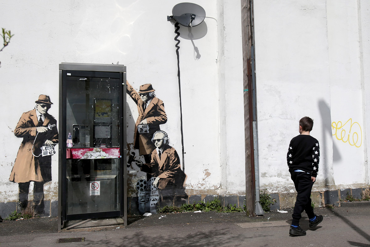 A boy walks past a possible Banksy graffiti which has appeared on the side of a house in Cheltenham, Gloucestershire. The artwork, which shows three figures listening into a conversation in a telephone box, is just a few miles away from Government Communications Headquarters (GCHQ)