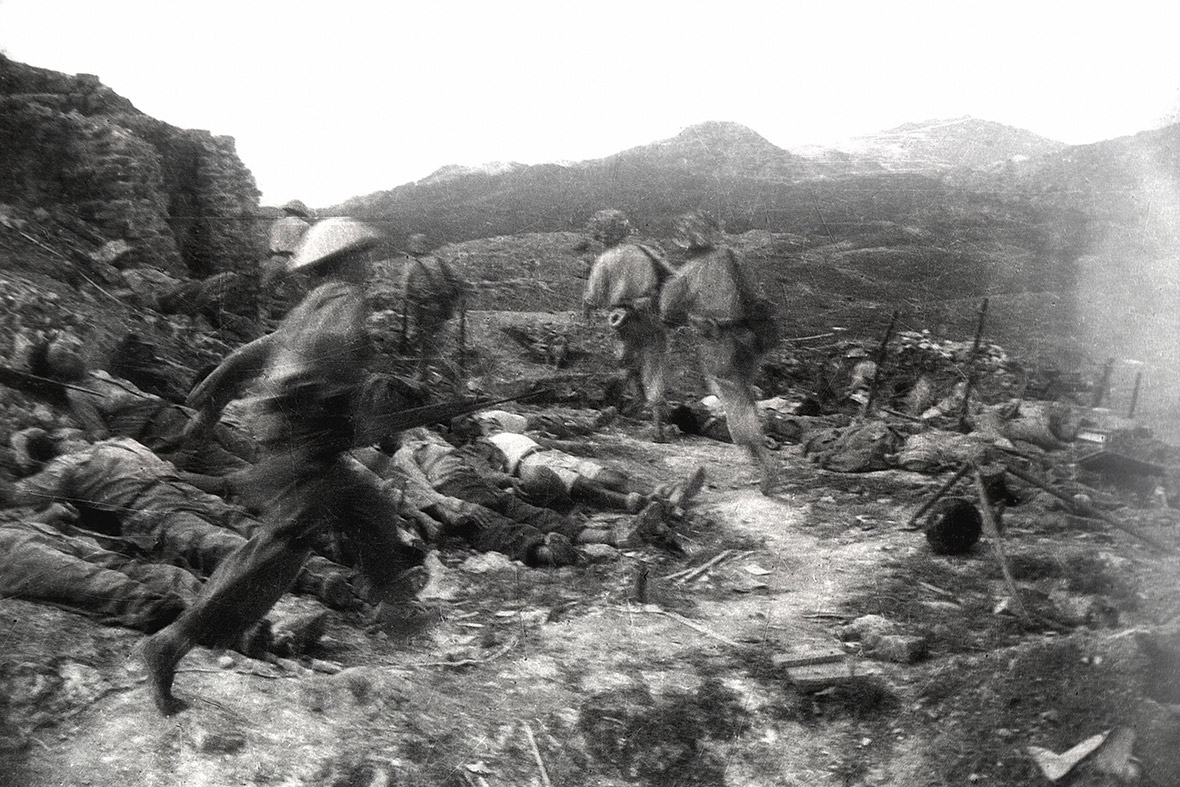 Vietnamese troops run past the bodies of French soldiers killed during an attack on a French stronghold on Eliane Hill