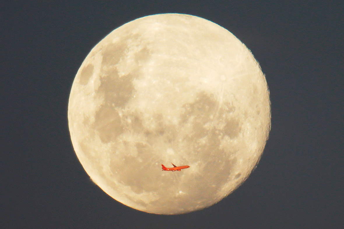 A Virgin Airlines commercial aircraft is illuminated by the setting sun in front of a full moon after taking off from Sydney Airport.