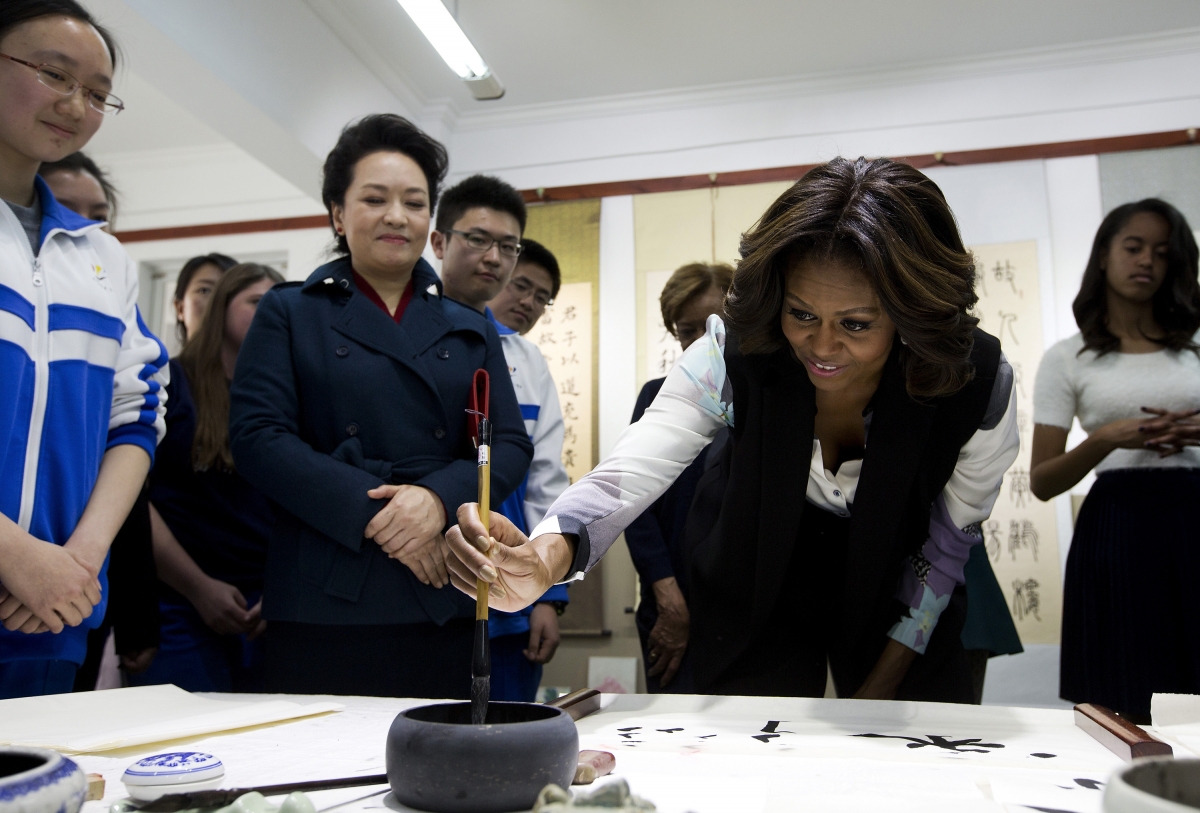 Michelle Obama tries to write Chinese words with a brush as Peng Liyuan looks on.