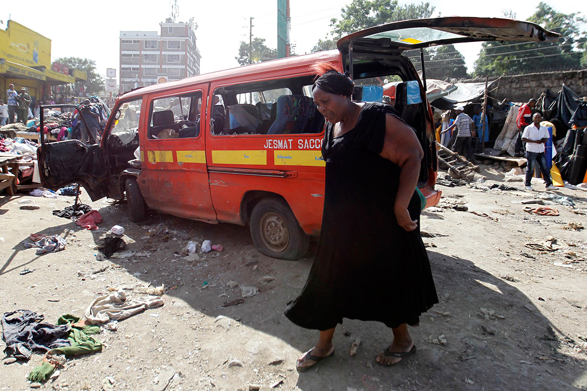 A woman walks near a damaged vehicle at the scene of twin explosions at the Gikomba open-air market in Nairobi