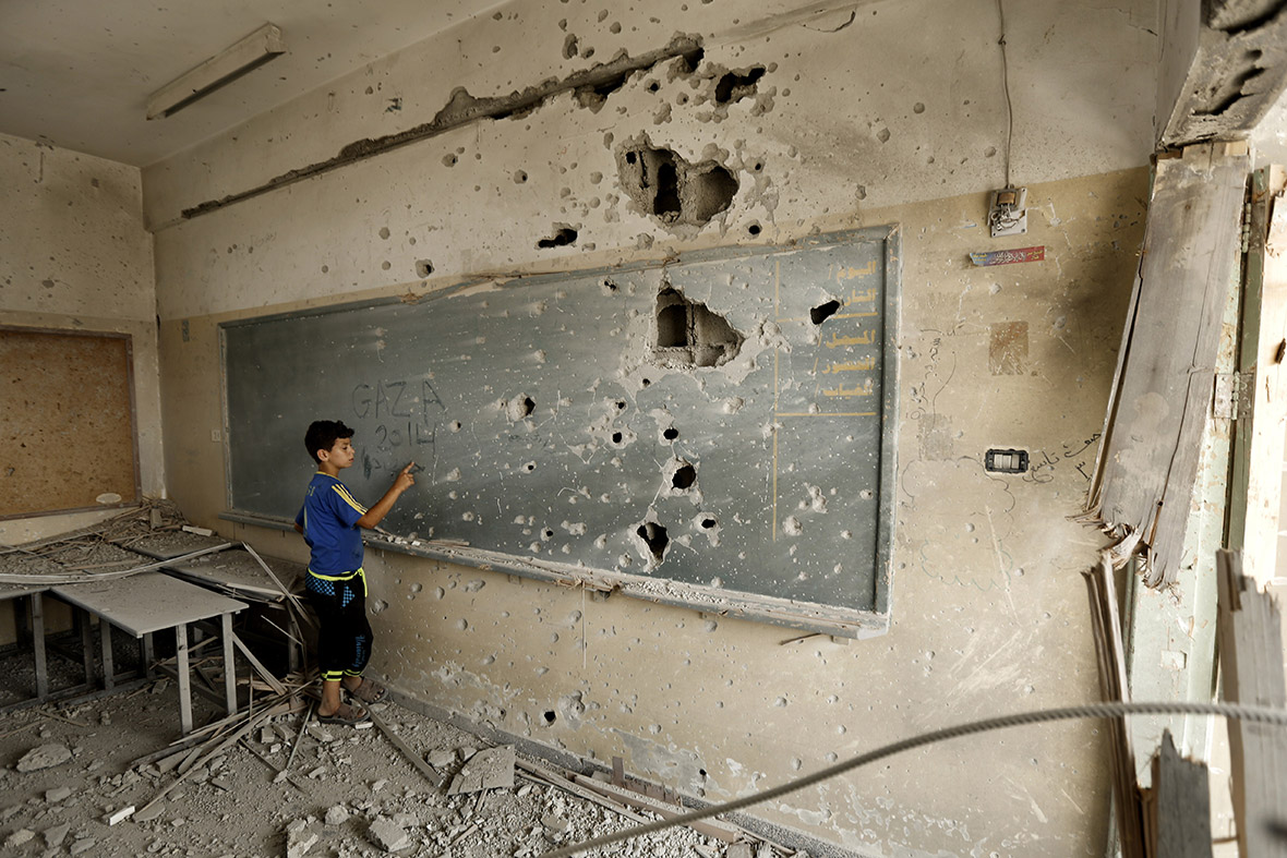 A Palestinian boy writes on a shrapnel-riddled backboard at the heavily damaged Sobhi Abu Karsh school in Gaza City's al-Shejaia neighbourhood