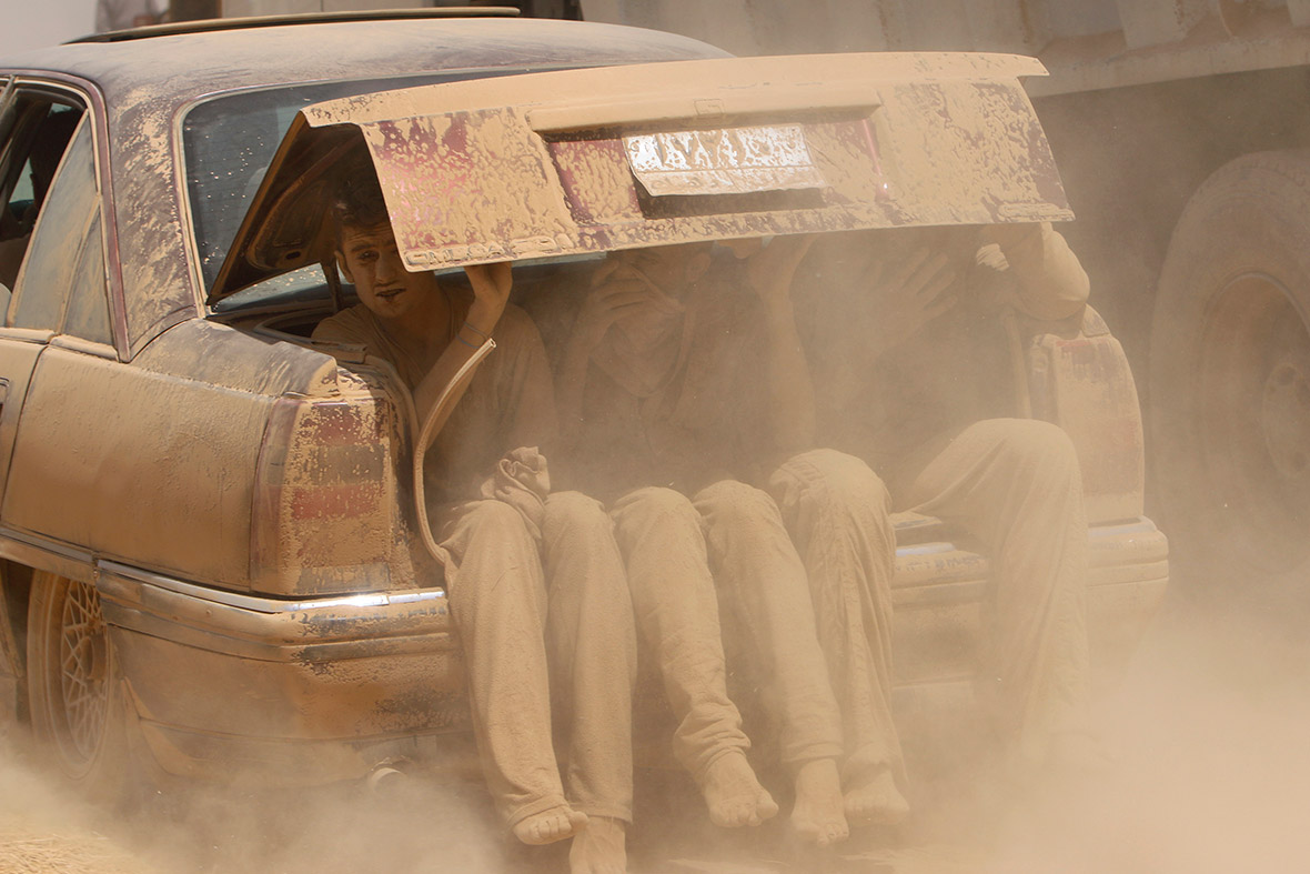 People covered in dust sit in the boot of a car as they flee the violence in Iraq and make their way towards the Syrian border