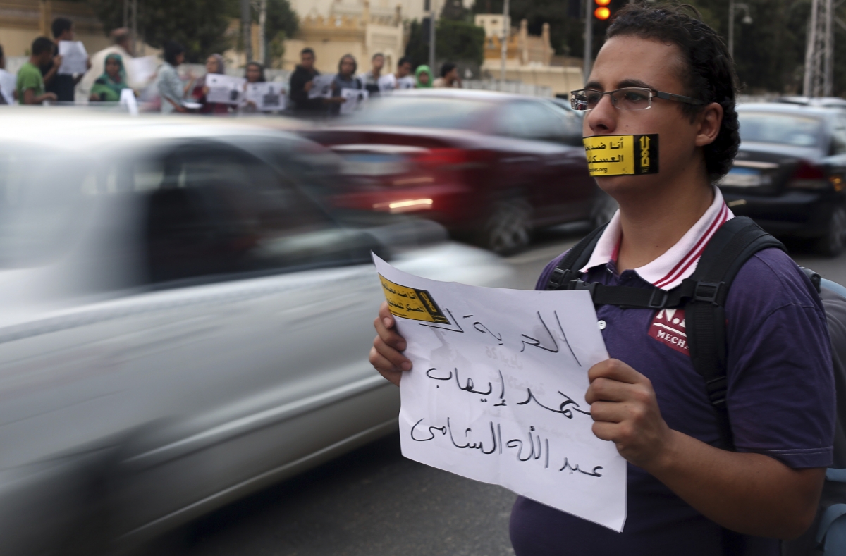 A demonstrator looks on with a sign reading