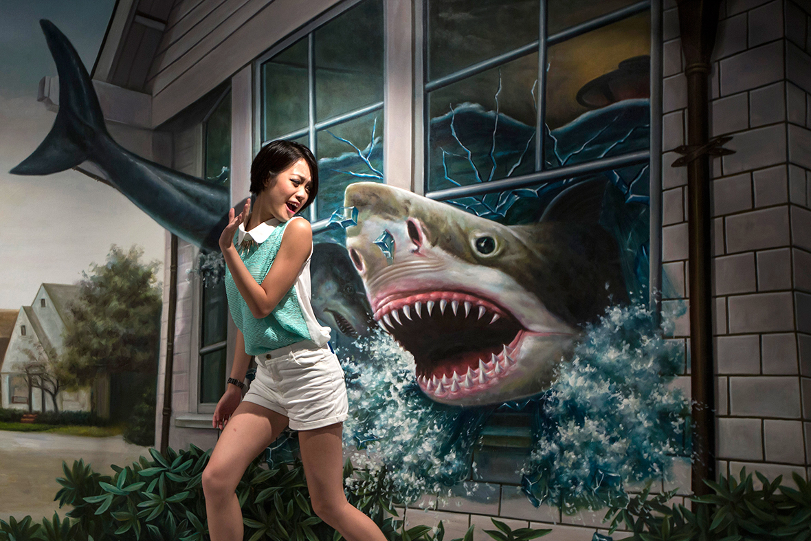 A woman poses for a photograph in front of a painting of a shark at HK 3D Museum in Hong Kong
