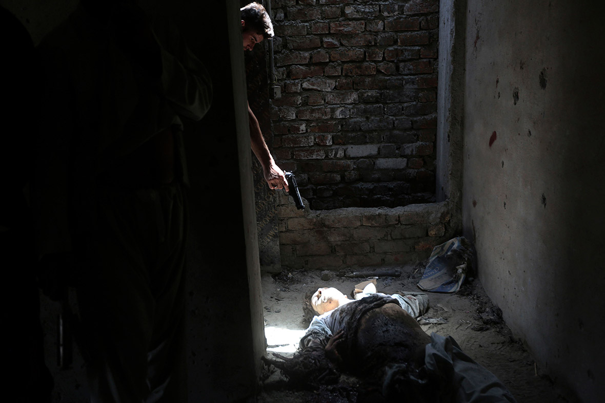 A member of the Afghan intelligence force points his pistol at the body of an insurgent