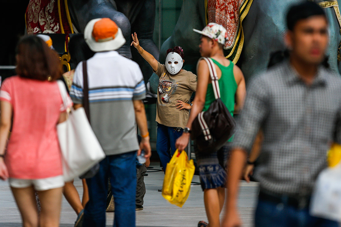 A masked demonstrator gives a three-fingered salute during a brief protest against military rule at a shopping mall in Bangkok