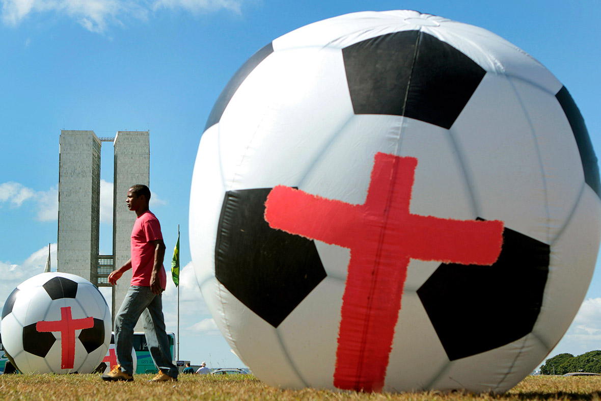 A man walks between giant inflatable footballs marked with red crosses in front of the National Congress in Brasilia during a protest calling for the Brazilian government to spend as much on education, health and public services as on World Cup stadiums