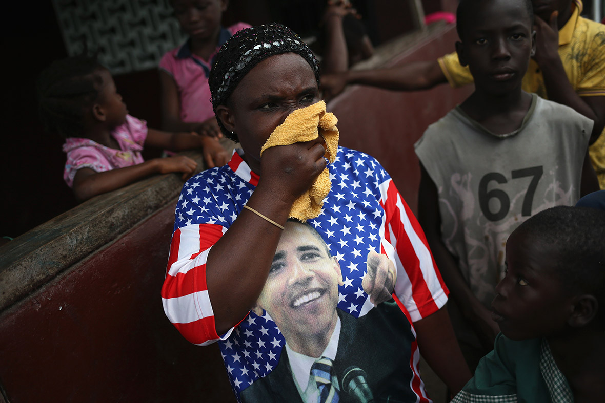 A woman wearing an Obama T-shirt covers her mouth and nose after protesters drove out an Ebola burial team who had come to collect the bodies of four people who had died overnight in the West Point slum
