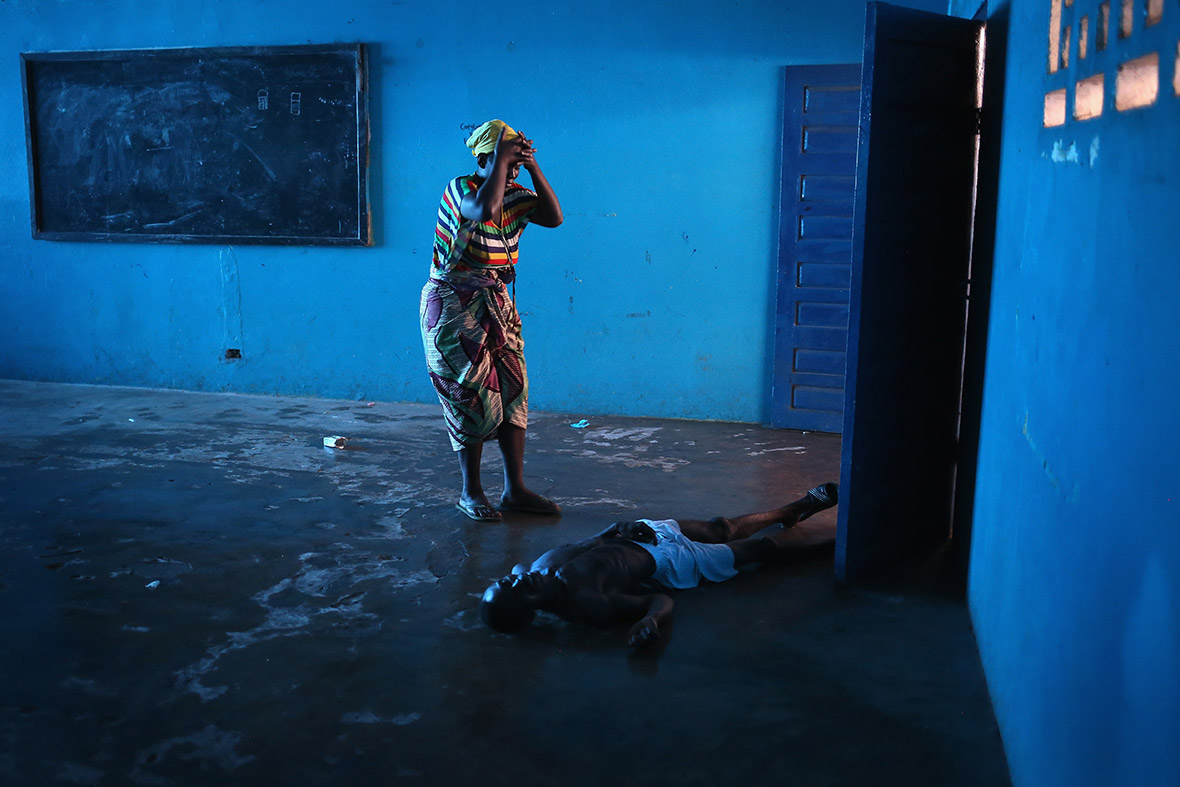 Umu Fambulle stands over her husband Ibrahim after he staggered and fell, knocking himself unconscious in an Ebola isolation centre in a closed primary school in Monrovia
