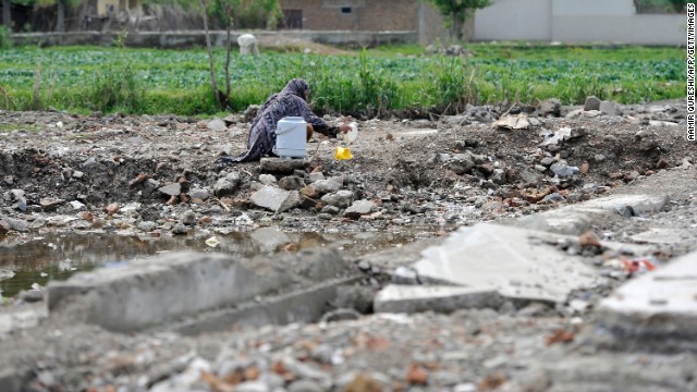 A Pakistani woman fills a container with water at the site of the demolished compound on April 25, 2012.