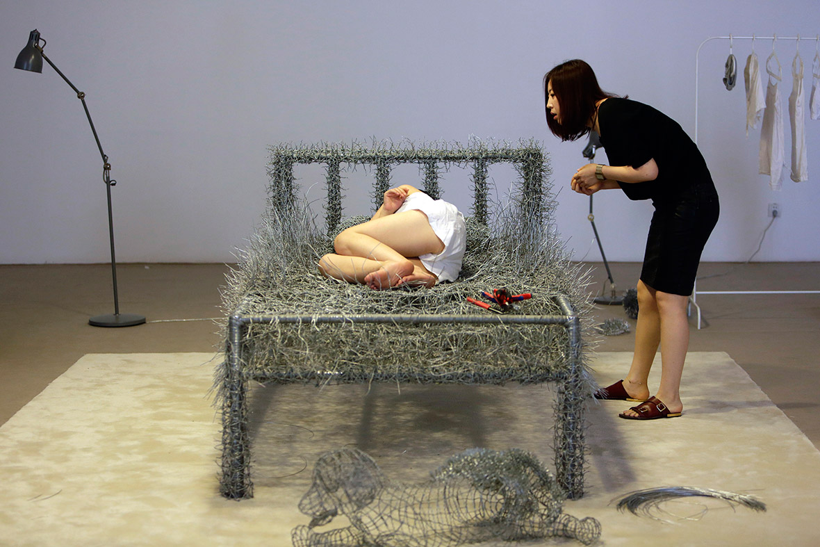 A woman watches Chinese artist Zhou Jie sleep on an unfinished iron wire bed, one of her sculpture works, at Beijing Now Art Gallery. The artist will live inside a gallery, producing wire sculptures and sleeping on her wire bed, for 36 days