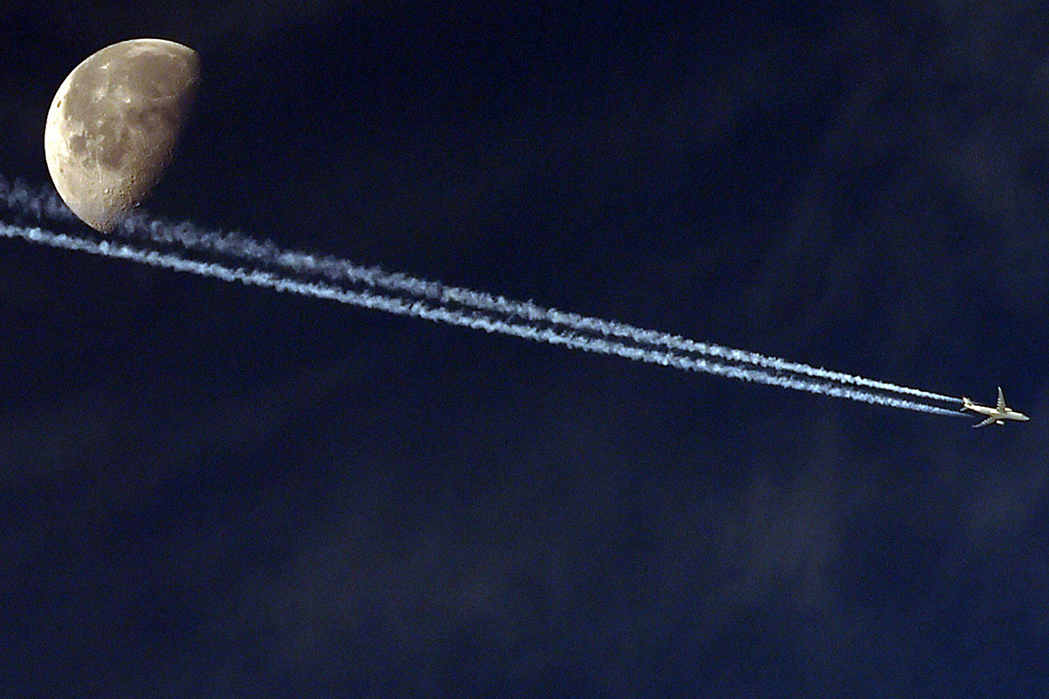 A jetliner leaves a vapour trail as it passes in front of the moon, as seen from the Algerian capital Algiers