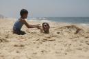 Palestinian boy buries his brother with sand as they play on a beach in the central Gaza Strip