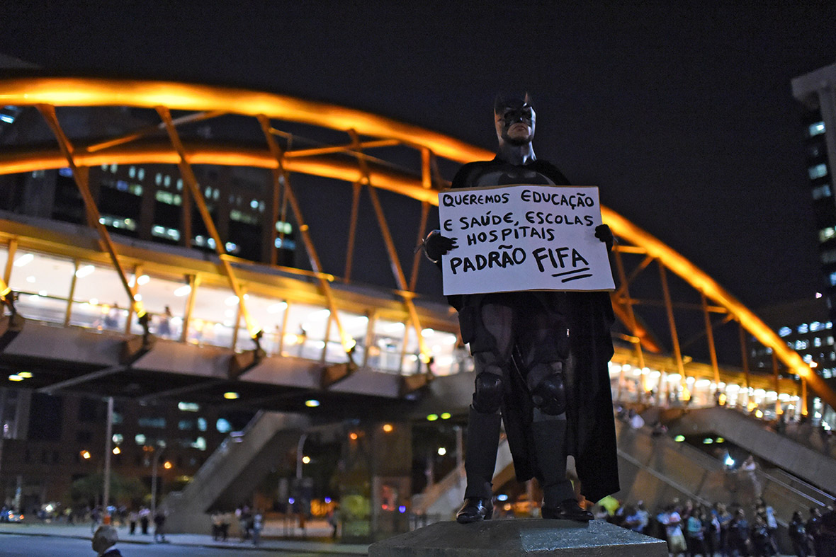 The Dark Knight holds a placard reading: 'We want education, health, schools and hospitals at Fifa standards' on 15 May 2014.