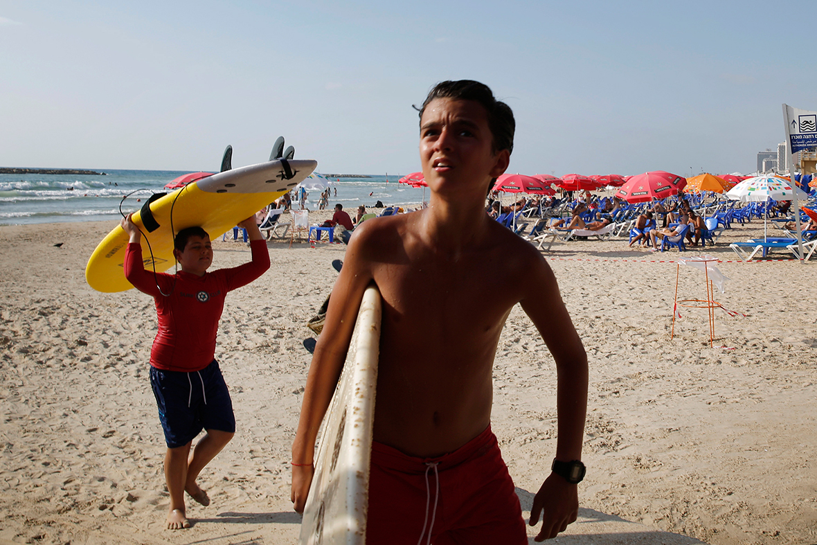 Boys carry their surf boards as their lesson is cancelled following a mid-air explosion as a rocket is intercepted by the Iron Dome defence system over Tel Aviv