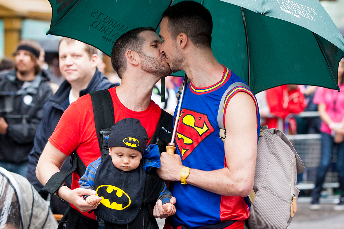 Two men with a baby share a kiss as they take part in the annual Pride In London parade