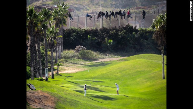 <strong>October 22:</strong> A golfer hits a tee shot as African migrants sit atop a border fence dividing Morocco and the Spanish enclave of Melilla.