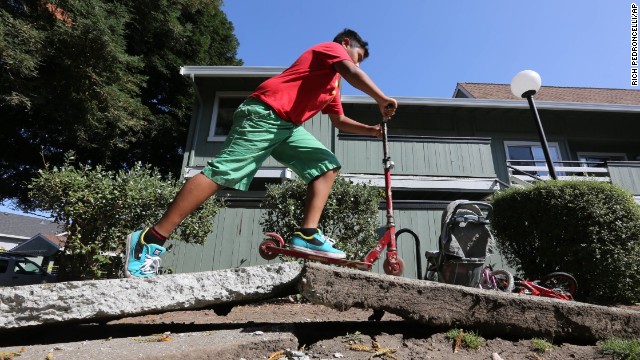 A boy rides a scooter over a sidewalk buckled by the earthquake on August 24 in Napa. 