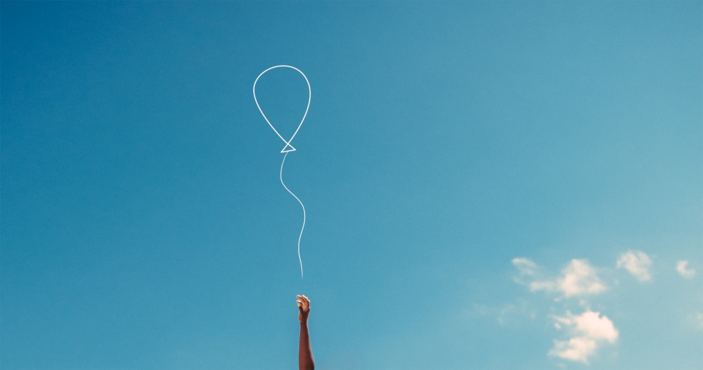 Womans Hand Reaching With Hope To Catch A Balloon Against Blue Sky