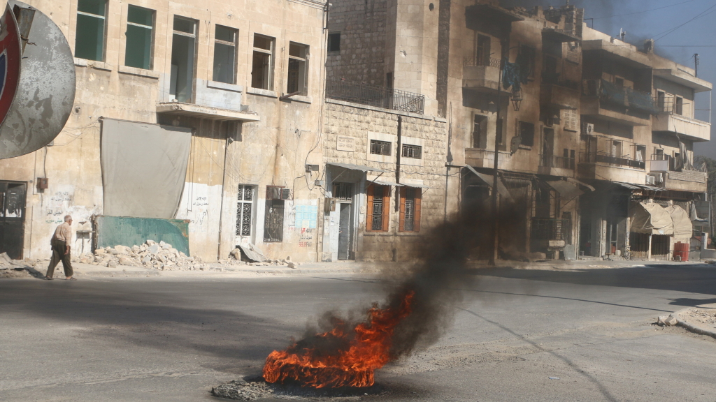 Ein Mann geht in der syrischen Stadt Aleppo an brennenden Autoreifen entlang. | Bildquelle: REUTERS