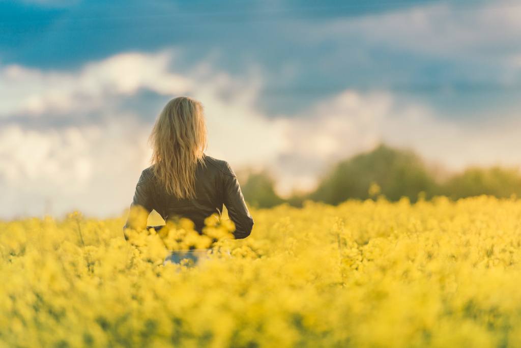 Girl Standing In Field Of Flowers At Sunset