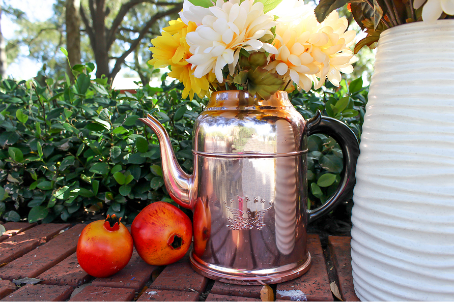 fall flowers displayed in a watering can outside among other fall nature elements. 