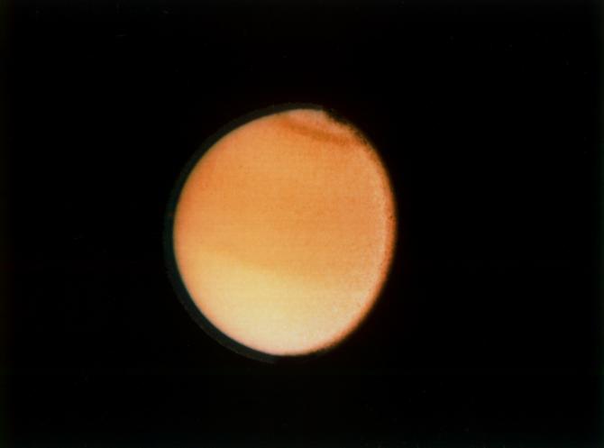 This Voyager 2 photograph of Titan, taken Aug. 23, 1981 from a range of 2.3 million kilometers (1.4 million miles), shows some detail in the cloud systems on this Saturnian moon. The southern hemisphere appears lighter in contrast, a well-defined band is seen near the equator, and a dark collar is evident at the north pole. All these bands are associated with cloud circulation in Titan's atmosphere. The extended haze, composed of submicron-size particles, is seen clearly around the satellite's limb. This image was composed from blue, green and violet frames.