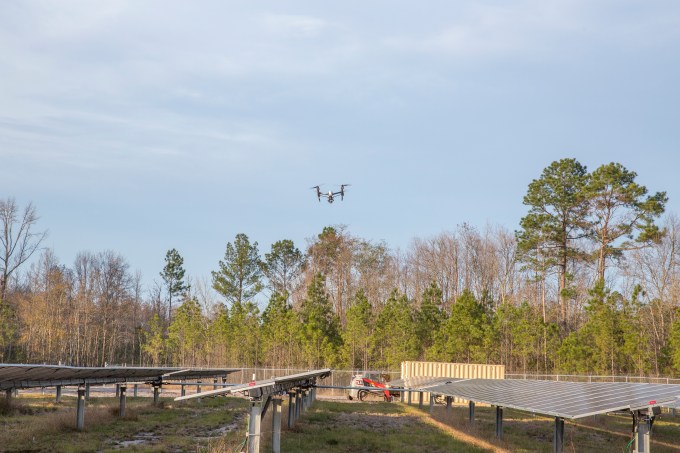 Measure flies drones to inspect solar panels in a field below.