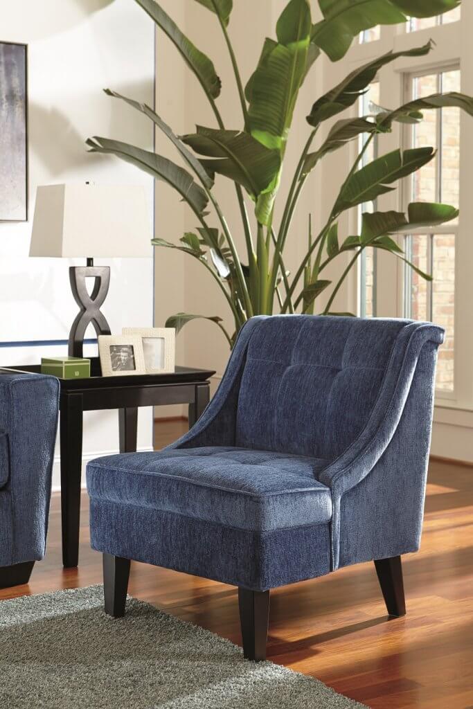 Blue fabric accent chair with an end table and lamp, and bamboo tree next to it. 