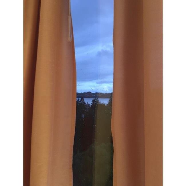 Blick aus einem Fenster durch einen Vorhangschlitz. Der orangefarbene Vorhang ist links und rechts sichtbar.