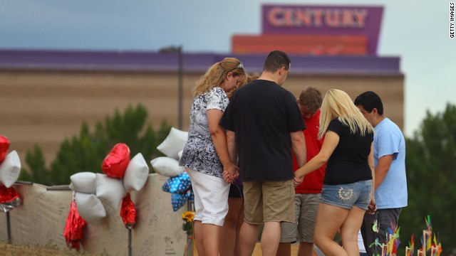 Visitors pray around a cross at the memorial across the street from the theater on Saturday, July 28.
