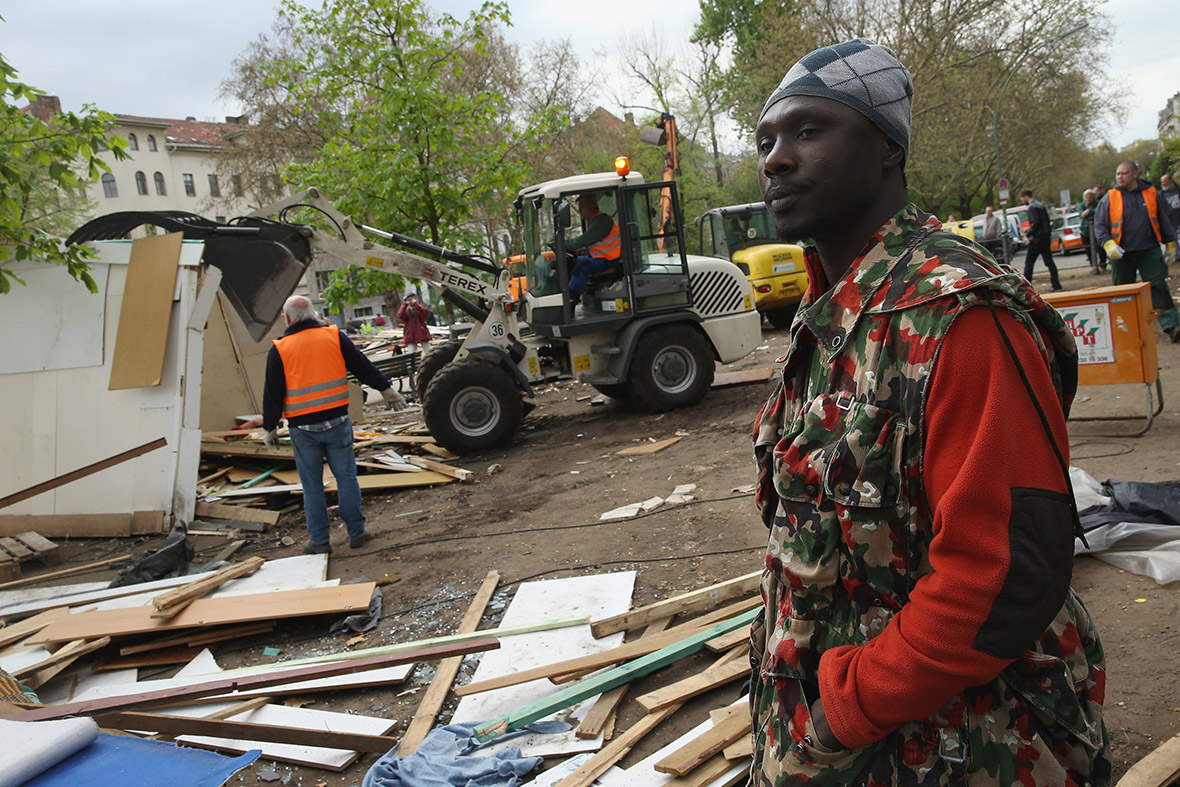 A refugee from Ghana who came to Germany via Libya and Lampedusa, and who has agreed to a deal with city authorities to move to a new shelter, stands by as huts are demolished