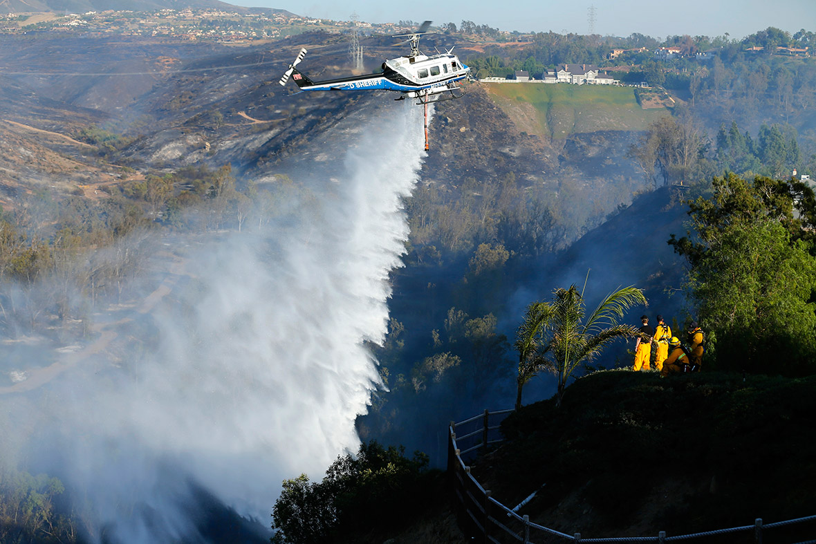 An helicopter drops water on a burning hillside as firefighters battle the Bernardo Fire, north of San Diego, California