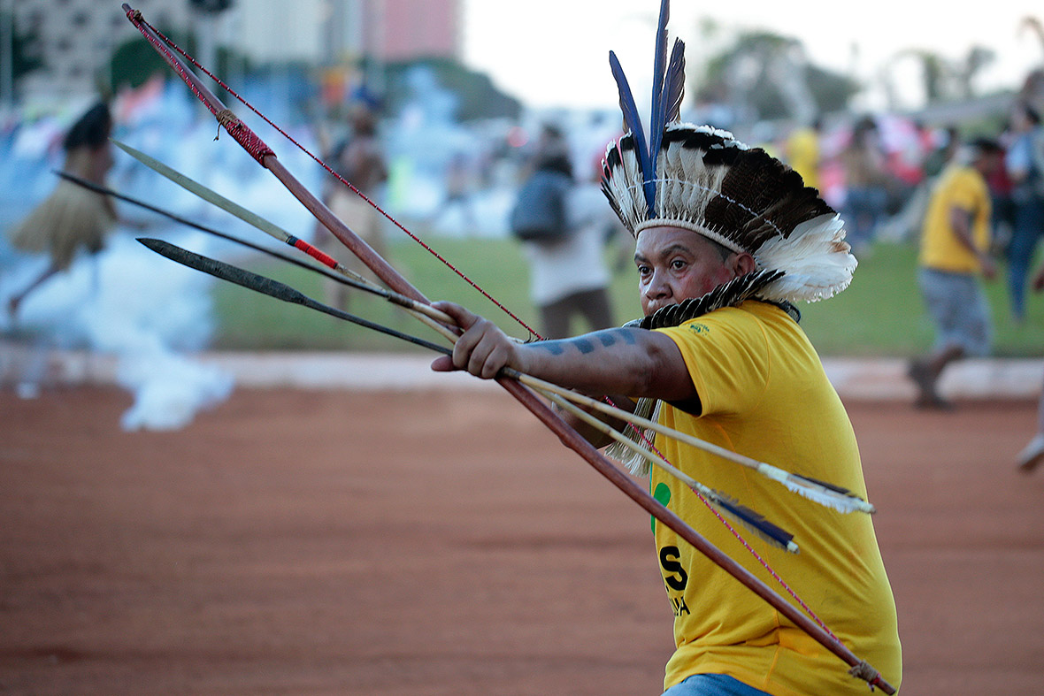 An indigenous Brazilian aims an arrow at riot police who fired tear gas at protesters