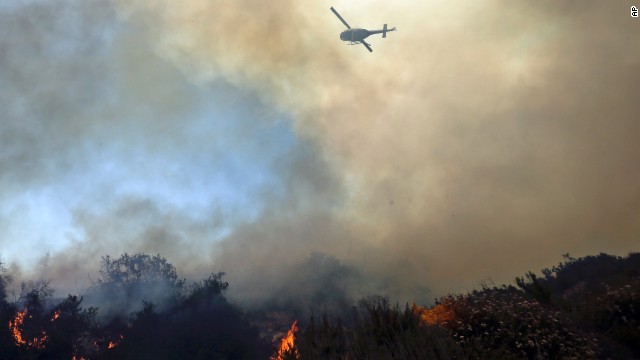 A helicopter flies over burning vegetation near homes in Carlsbad, California, on Wednesday, May 14. A couple of wildfires have forced evacuations in San Diego County after a high-pressure system brought unseasonable heat and gusty winds to the parched state.