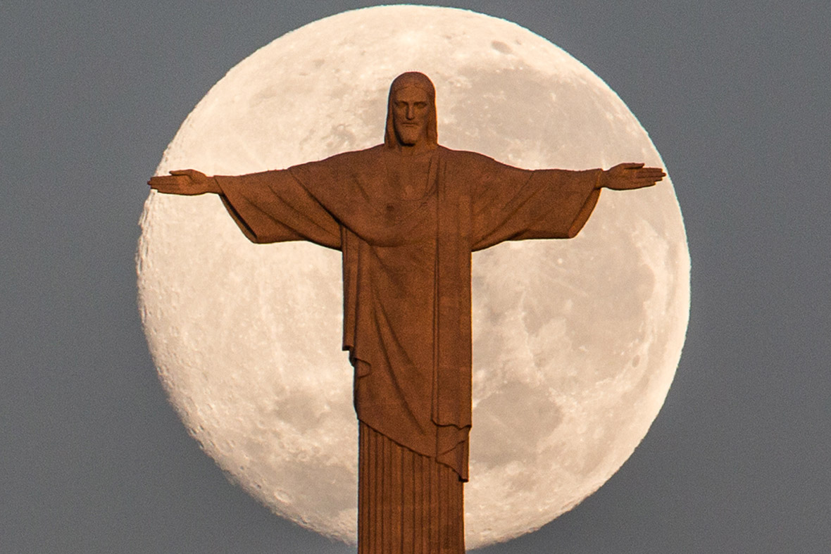 The moon sets behind the statue of Christ the Redeemer atop Corcovado hill in Rio de Janeiro, Brazil
