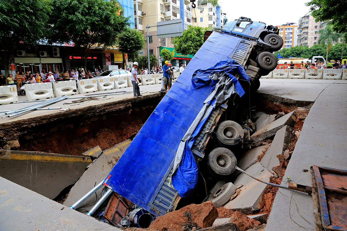 Workers stand next to a lorry that fell into a large pit caused by a cave-in on a street in Wuzhou, Guangxi Zhuang Autonomous Region, China