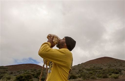 FILE - In this Aug. 31, 2015 file photo, Kupono Mele-Ana-Kekua, of Kaaawa, Hawaii, blows a conch shell near the summit of Mauna Kea on Hawaii's Big Island. Mele-Ana-Kekua had been camping on the mountain for about in protest of the Thirty Meter Telescope.  The Hawaii Supreme Court on Wednesday, Dec. 2, invalidated a permit awarded for the construction of one of the world’s largest telescopes on a mountain many Native Hawaiians consider sacred. (AP Photo/Caleb Jones, File)