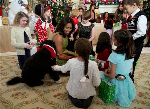 First lady Michelle Obama with dogs Bo, left, and Sunny, behind at right, are surrounded by children in the State Dining Room of the White House in Washington, Wednesday, Dec. 2, 2015, where they made holiday crafts and treats during a preview of the 2015 White House holiday decor. (AP Photo/Carolyn Kaster)